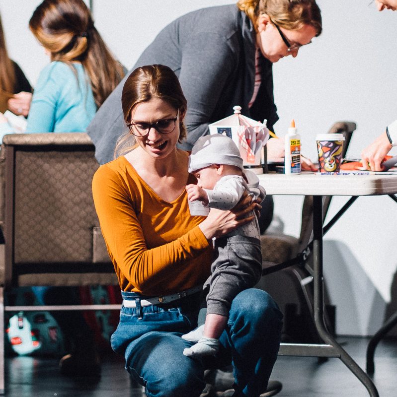 A mom holding her baby at the craft tables during a Tidal Moms morning