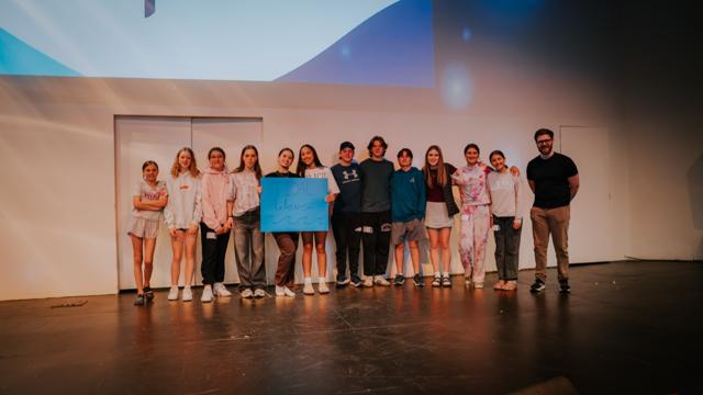 A small group of Tidal Youth students posing on stage with a sign