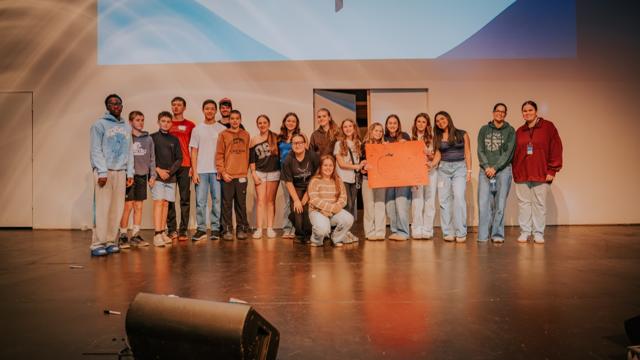 Tidal Youth students and leaders posing on stage with a poster